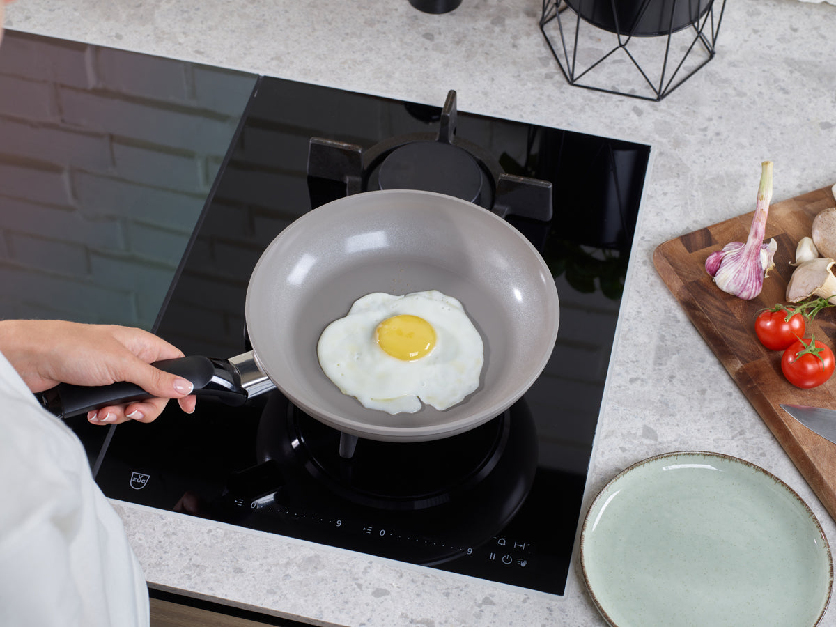 Kochen eines Spiegeleis in einer Fissler Ceratal Classic Pfanne, mit frischen Zutaten und modernem Design auf einer eleganten Arbeitsplatte.