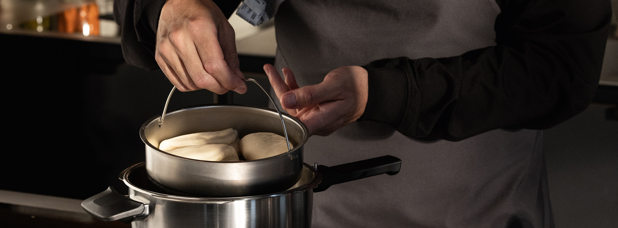 Ein Koch in grauer Schürze hebt frischen Teig aus einem Fissler-Edelstahltopf, der für deutsche Qualität und innovatives Design steht.