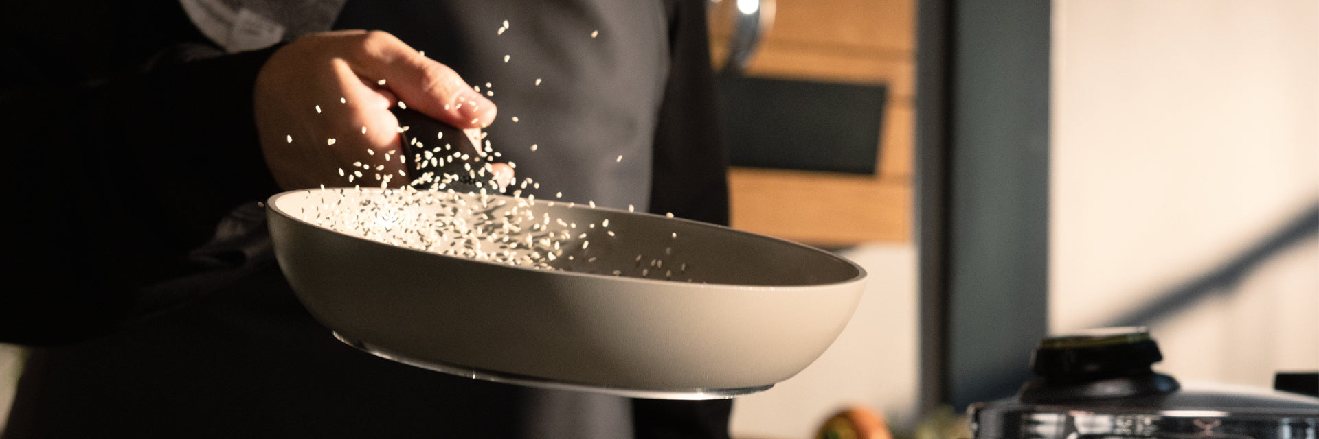 Ein Koch schwenkt gekonnt Reis in einer Fissler-Pfanne, Körner in der Luft, vor einem sanft beleuchteten Küchenhintergrund - Präzision und zeitloses Design.