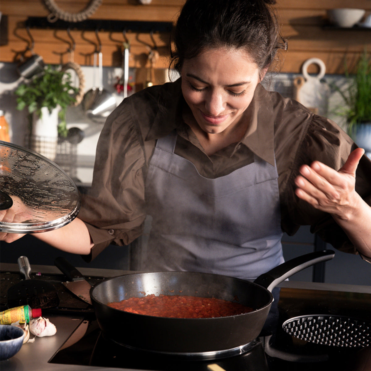 A woman smiles, lifting the lid on Fissler Ceratal® Evo Comfort pans, savoring "Made in Germany" quality and timeless design.