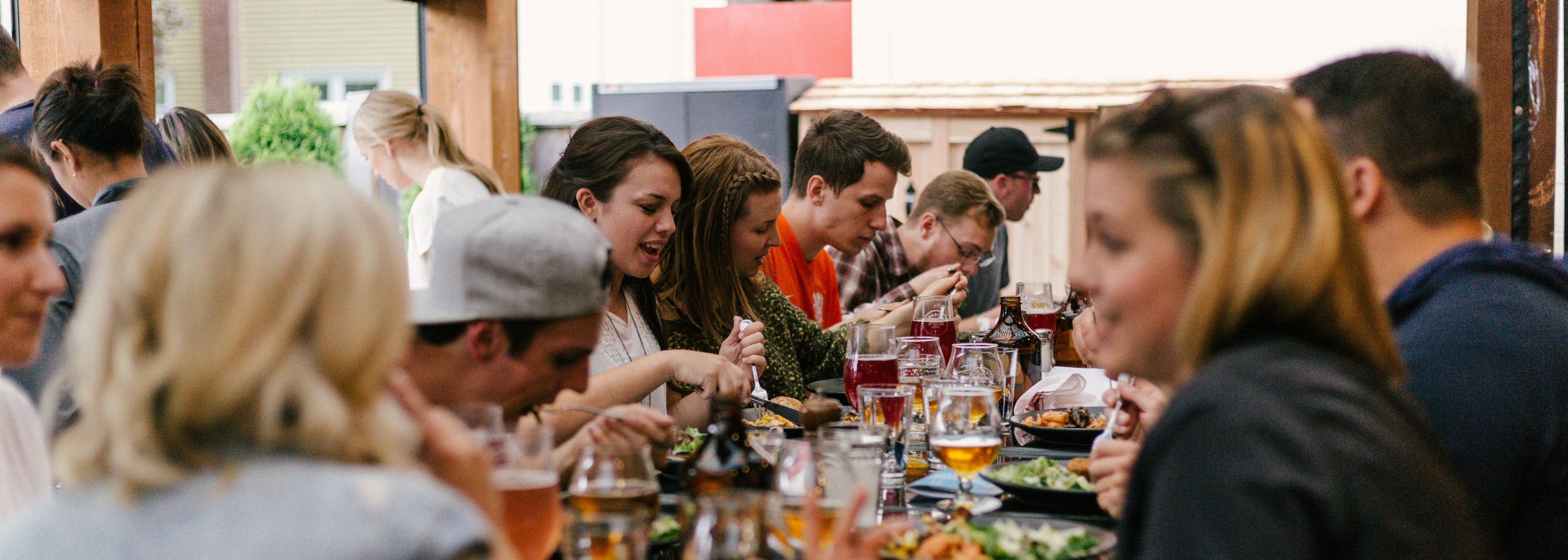 Friends gather around a long outdoor table, sharing food from Fissler stainless steel cookware and chatting animatedly.