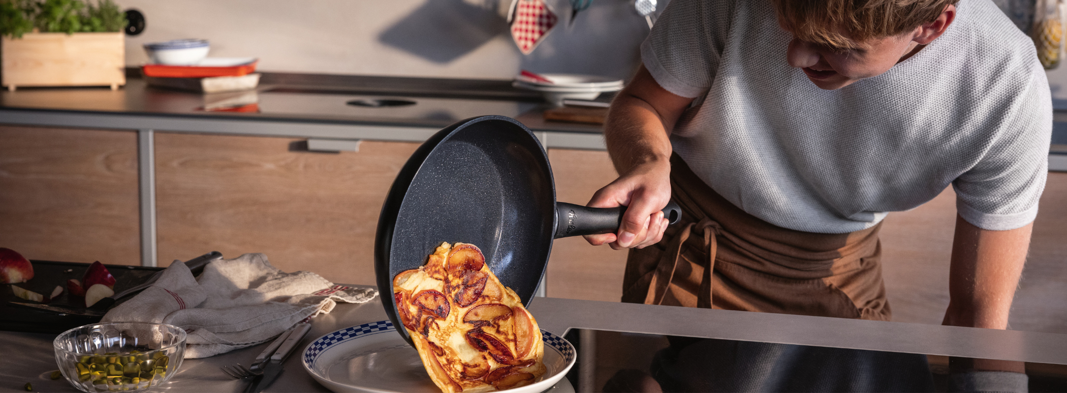 A person expertly slides a golden omelet from a Fissler pan onto a plate; high-quality cookware and utensils are on the countertop.