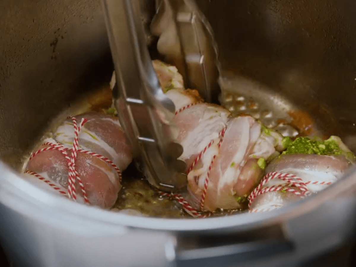 Bacon-wrapped chicken breasts are seared in a Fissler stainless steel pot held with tongs - precision, quality "Made in Germany."