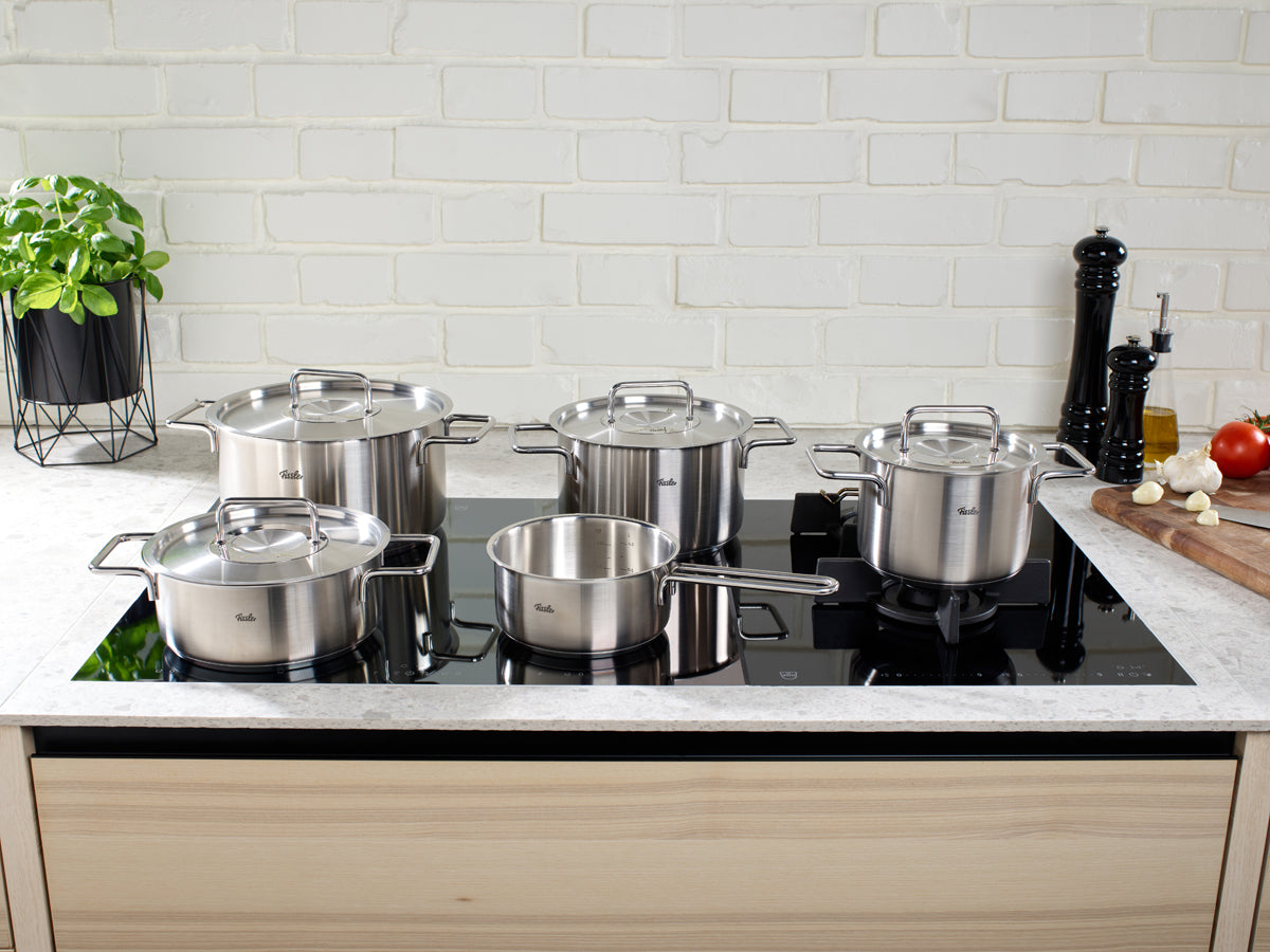 Fissler Pure Collection® pots and Ceratal® Evo Comfort Pan 24 cm on a black induction hob; modern kitchen, fresh herbs, vegetables.