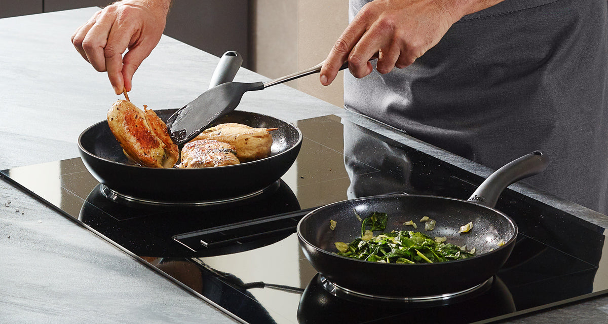 The chicken breast is pan-fried in a Fissler Essential® pan with a stainless steel spatula, while the vegetables are sautéed in another "Made in Germany" precision pan.