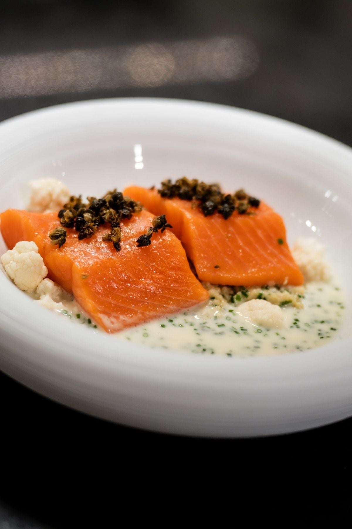 Perfekt gekochter Lachs mit Kapern und Blumenkohl auf cremiger Kräutersauce, elegant serviert in einer weißen Schale - in Fissler-Qualität.