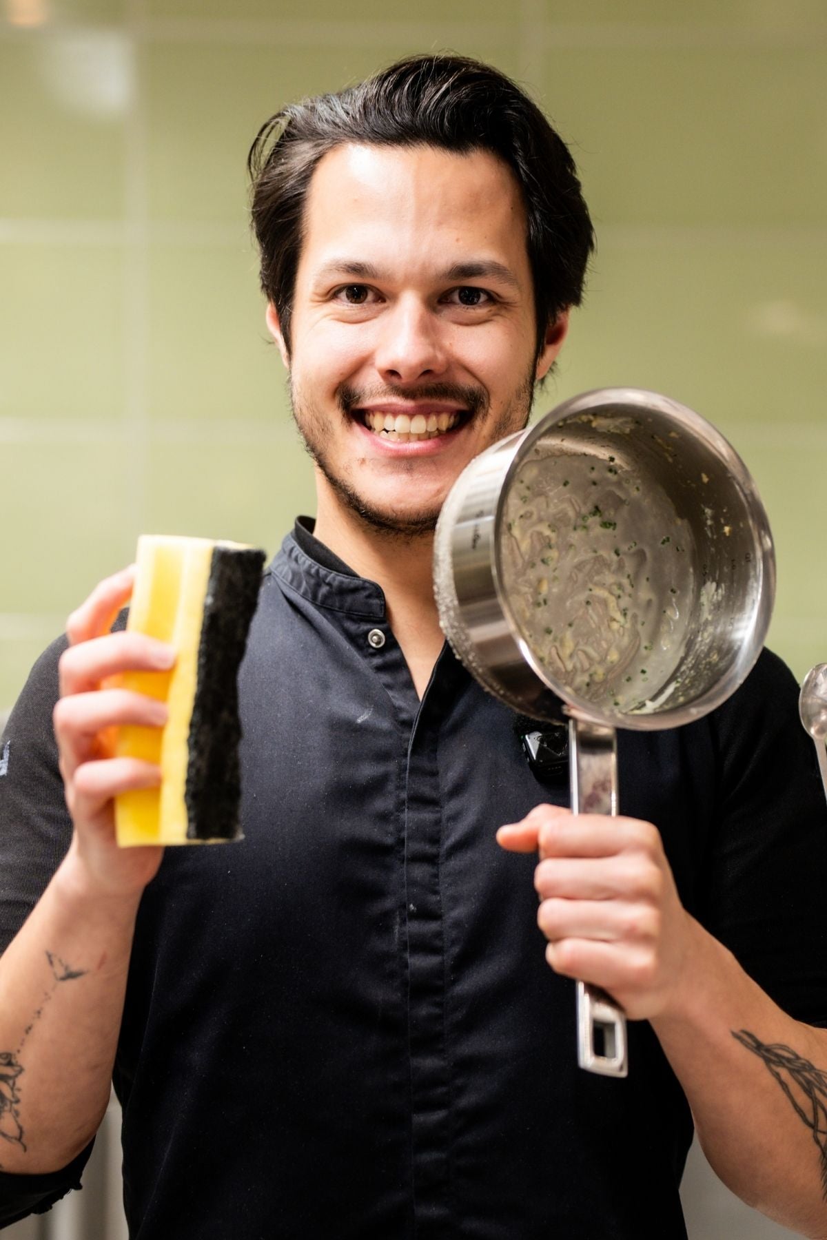 Ein lächelnder Koch in Uniform steht in einer modernen Küche und ist bereit, einen Fissler-Topf zu reinigen, der für deutsche Qualität und Innovation steht.