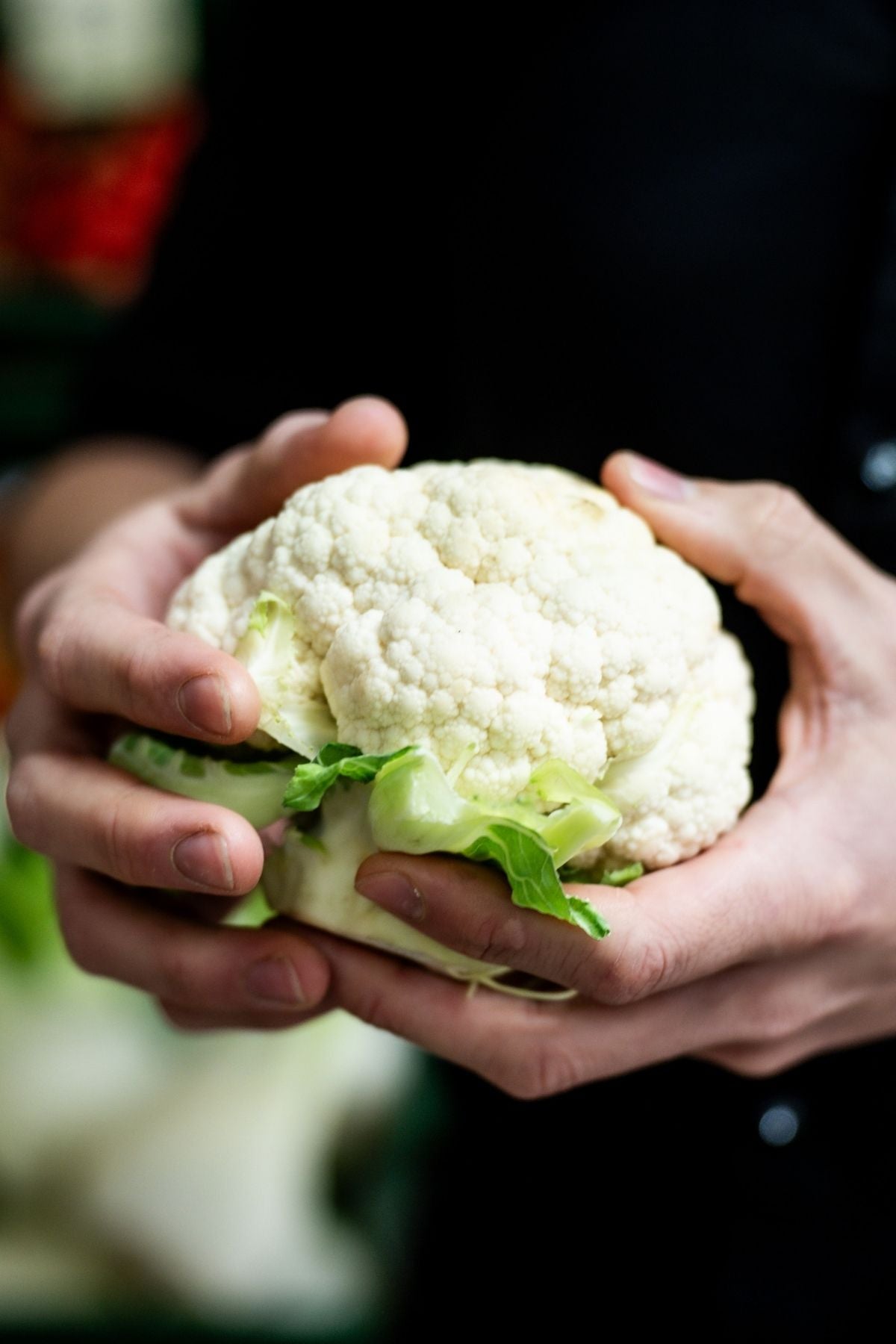 Eine Person in einem dunklen Hemd hält einen frischen Blumenkohl in der Hand, bereit für die Zubereitung mit dem deutschen Präzisionskochgeschirr von Fissler.