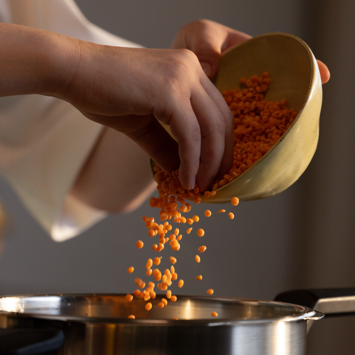 A person pours red lentils from a yellow bowl into a premium Fissler stainless steel pot on a stovetop, highlighting the durability and timeless design of Fissler’s German-engineered cookware.