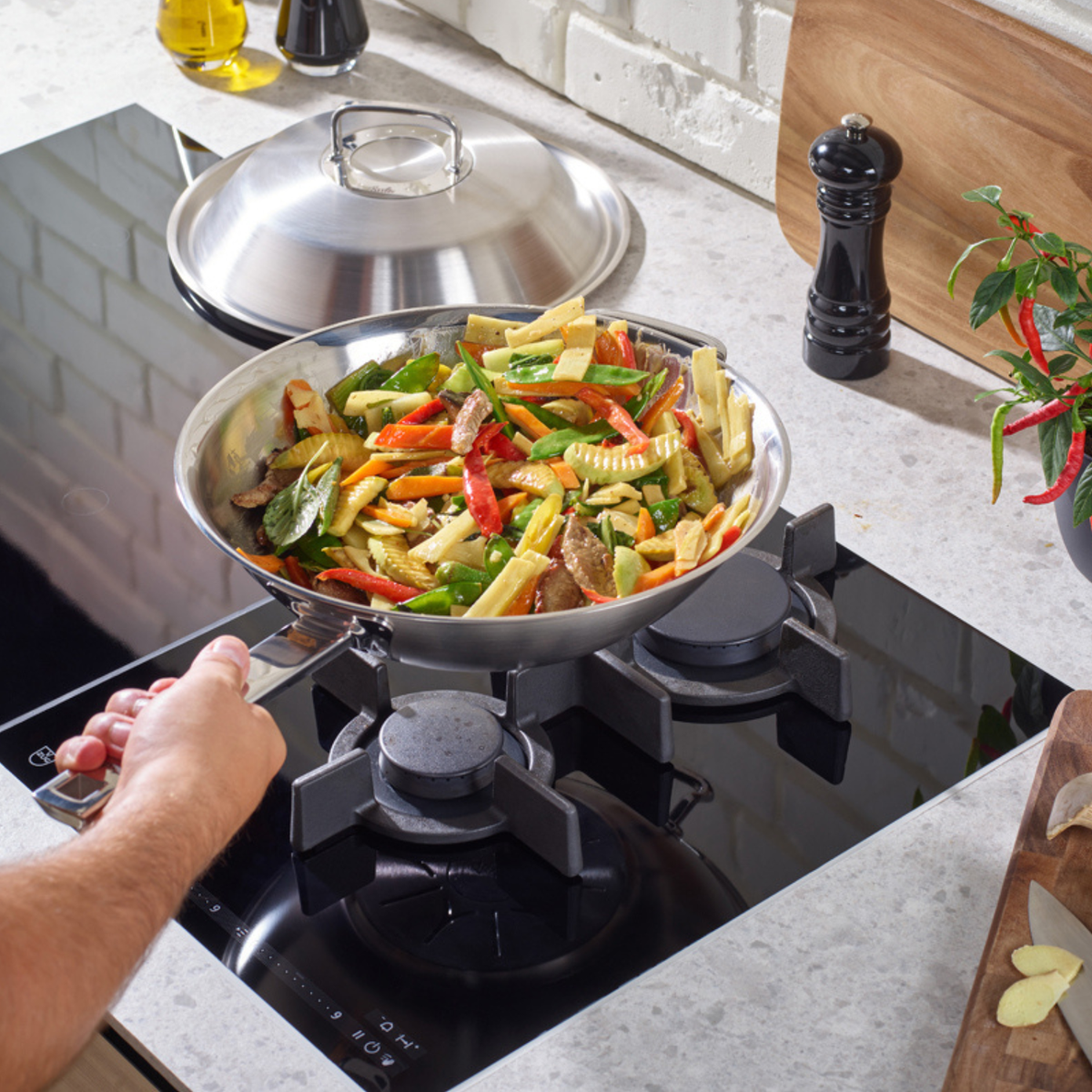 A person prepares a vibrant vegetable stir-fry in a premium Fissler stainless steel pan on a gas stove, with sliced fresh vegetables arranged on a cutting board nearby—showcasing the precision engineering and timeless design of Fissler cookware.