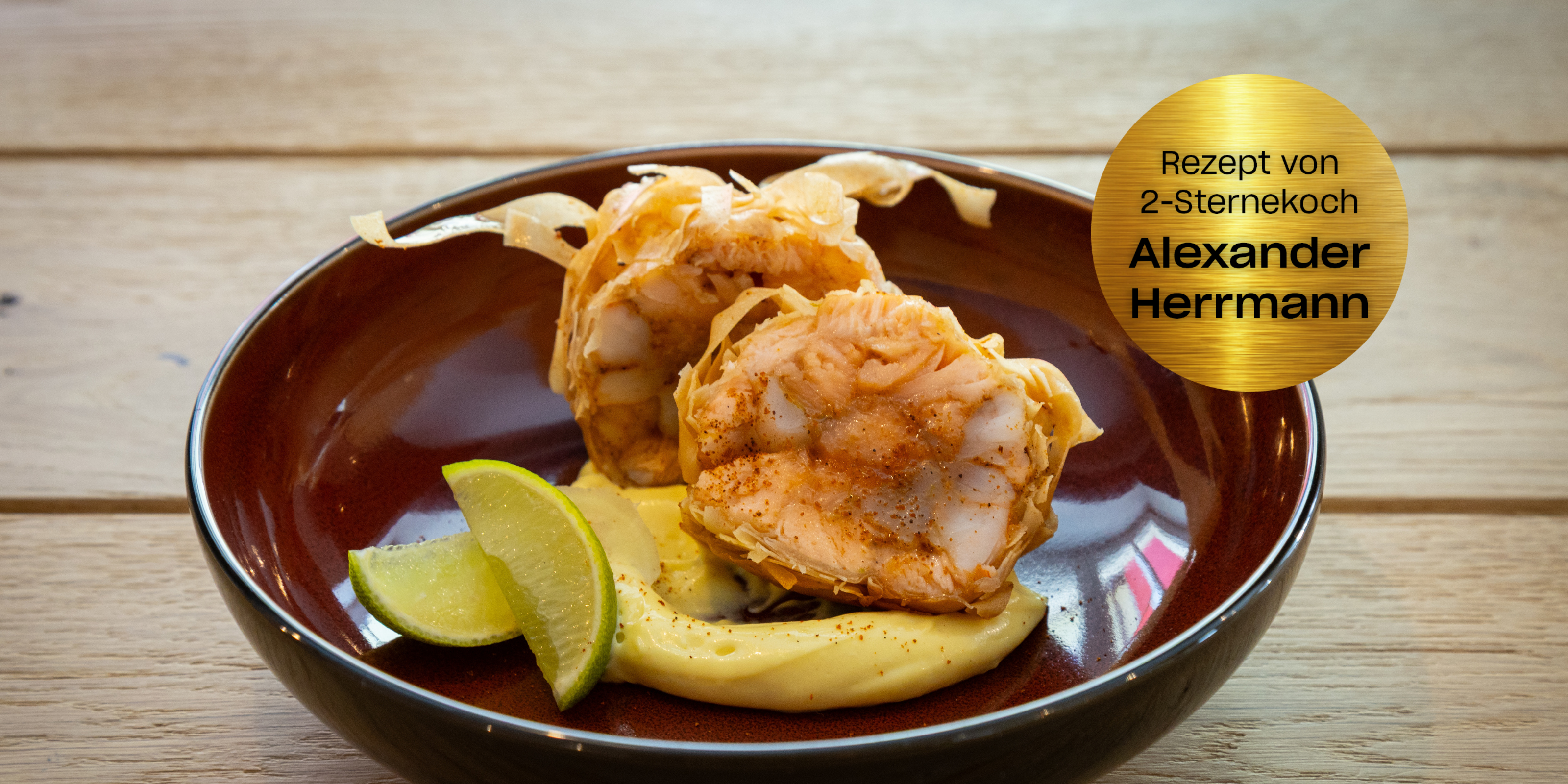 Zwei Meeresfrüchtepakete in Sahnesauce mit Limette, präsentiert in einer Schale auf Holz. Goldene Plakette: Rezept von 2-Sternekoch Alexander Herrmann.