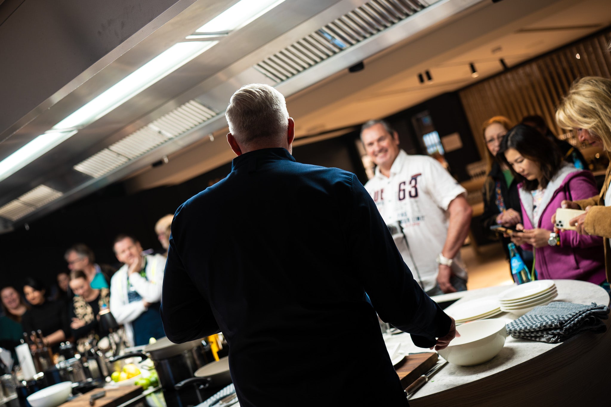 A chef demonstrates in a modern kitchen with Fissler stainless steel cookware as guests watch and chat around the counter.