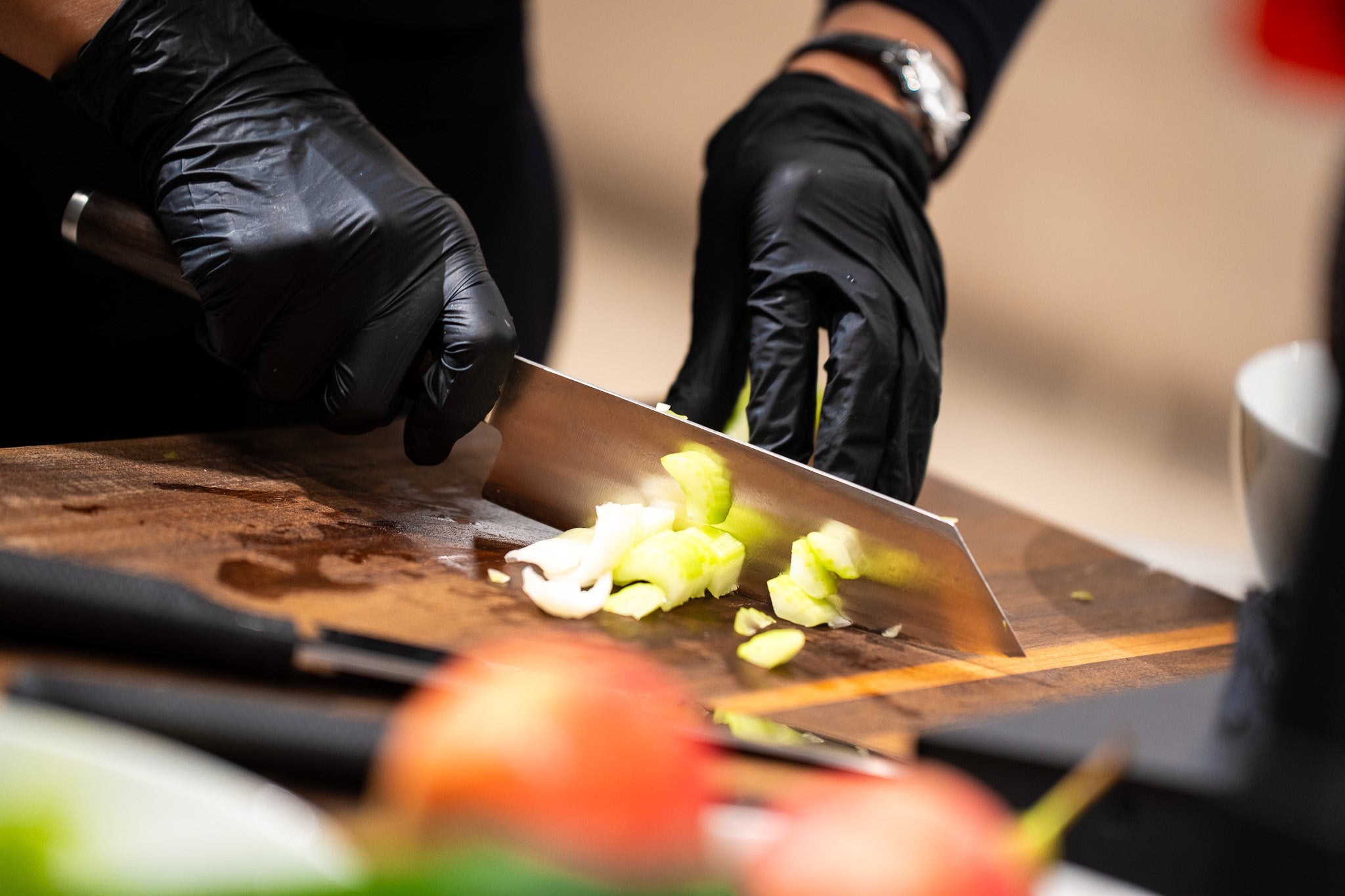 A person in black gloves cuts celery on a wooden board with a Fissler chef's knife. High-quality cookware is in the foreground.