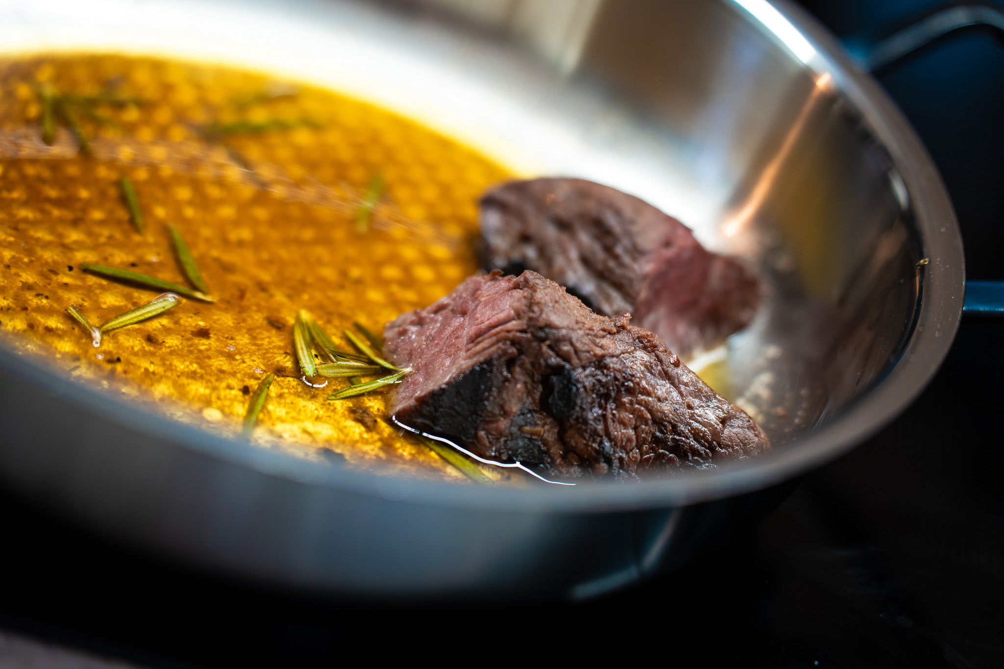 Perfectly roasted meat with rosemary in a golden-brown sauce, presented in a high-quality Fissler stainless steel pan.