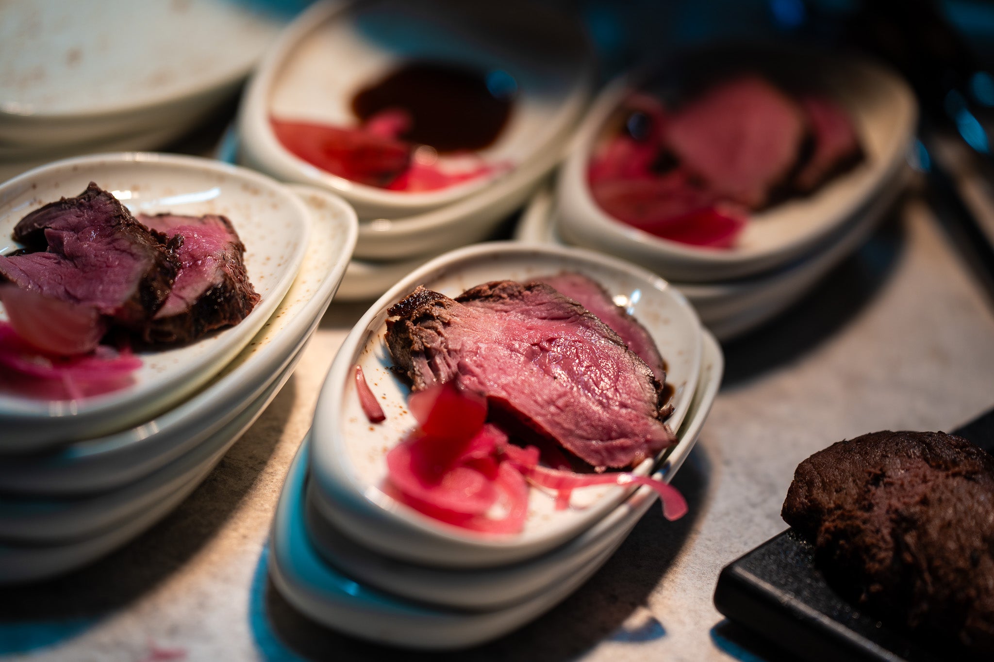 Half-cooked roast beef with pickled onions on white plates, elegantly arranged on a countertop next to Fissler cookware.