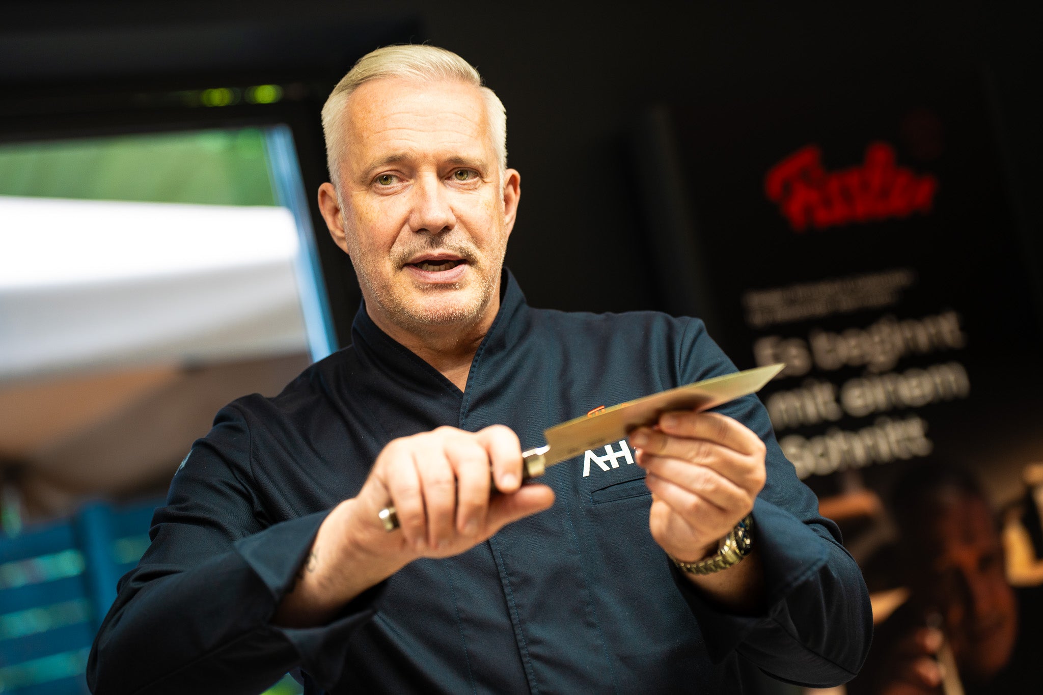 A chef in a dark jacket presents a high-quality Fissler kitchen knife, highlighting German precision and quality in a bright home kitchen.