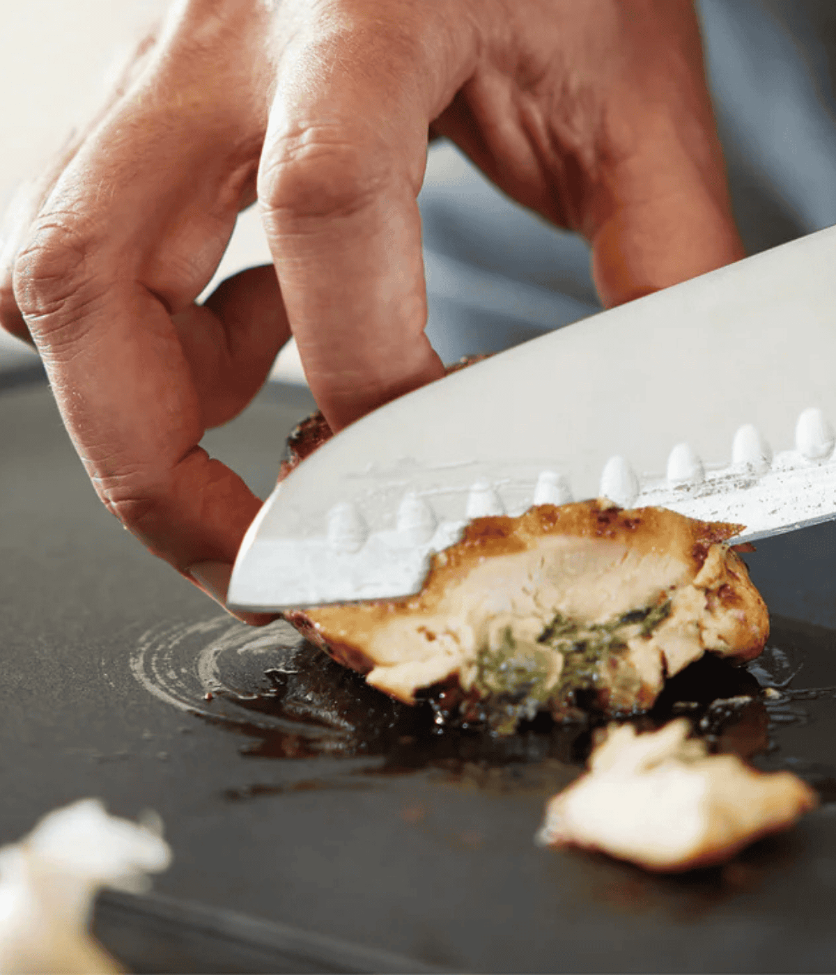 A hand expertly slices stuffed chicken on a cutting board with a Fissler chef's knife, showcasing precision and high-quality cookware.
