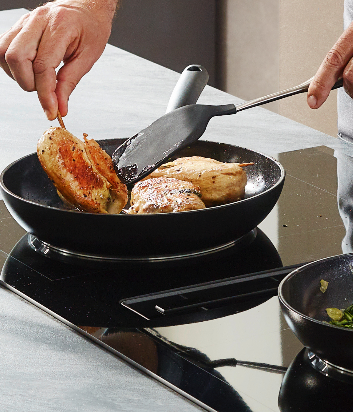 A chef prepares a stuffed chicken in an elegant Fissler pan on an electric stove; next to it is a Fissler pan with fresh greens.